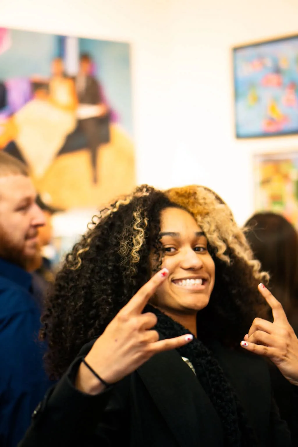 Diany grinning and throwing up rock-on hands at a gallery opening
